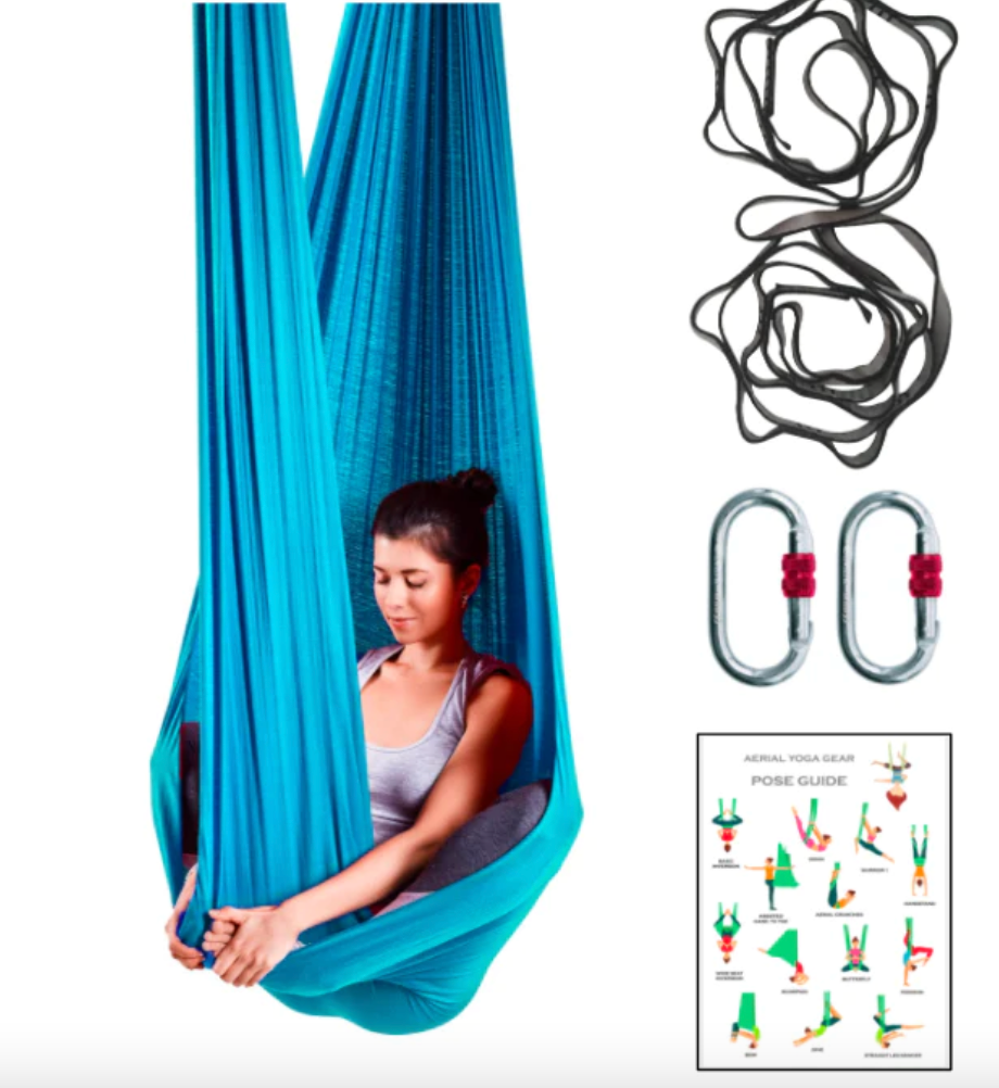 A woman hanging in a blue aerial yoga hammock with the rigging equipment on her right side. 