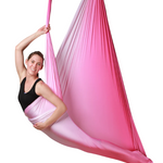 A woman hanging from a pink ombre aerial hammock.