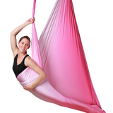 A woman hanging from a pink ombre aerial hammock.