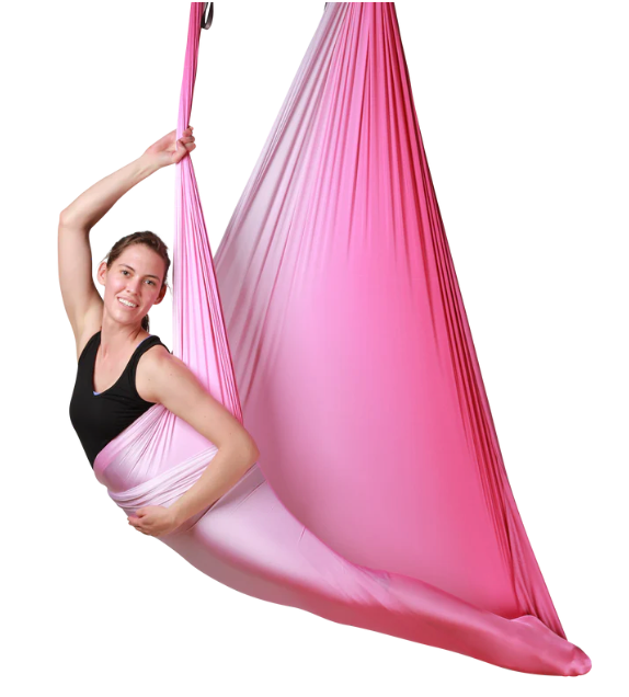 A woman hanging from a pink ombre aerial hammock.