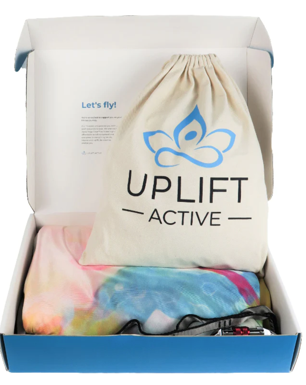 A box with the aerial hammock and rigging equipment. The box includes a beige bag with “Uplift Active” on it and a tie dye hammock. 