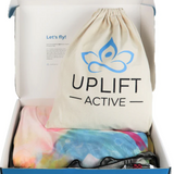 A box with the aerial hammock and rigging equipment. The box includes a beige bag with “Uplift Active” on it and a tie dye hammock. 