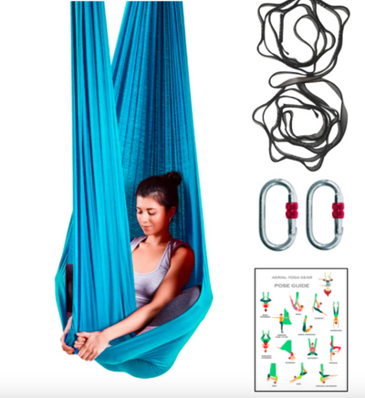A woman hanging in a blue aerial yoga hammock with the rigging equipment on her right side. 